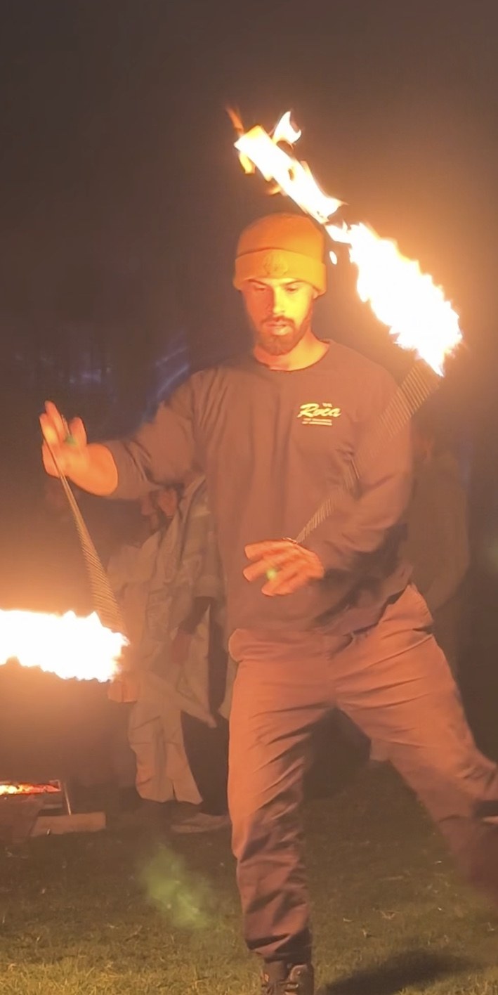 Jono Mitchell performing front-facing fire poi at a live nighttime event