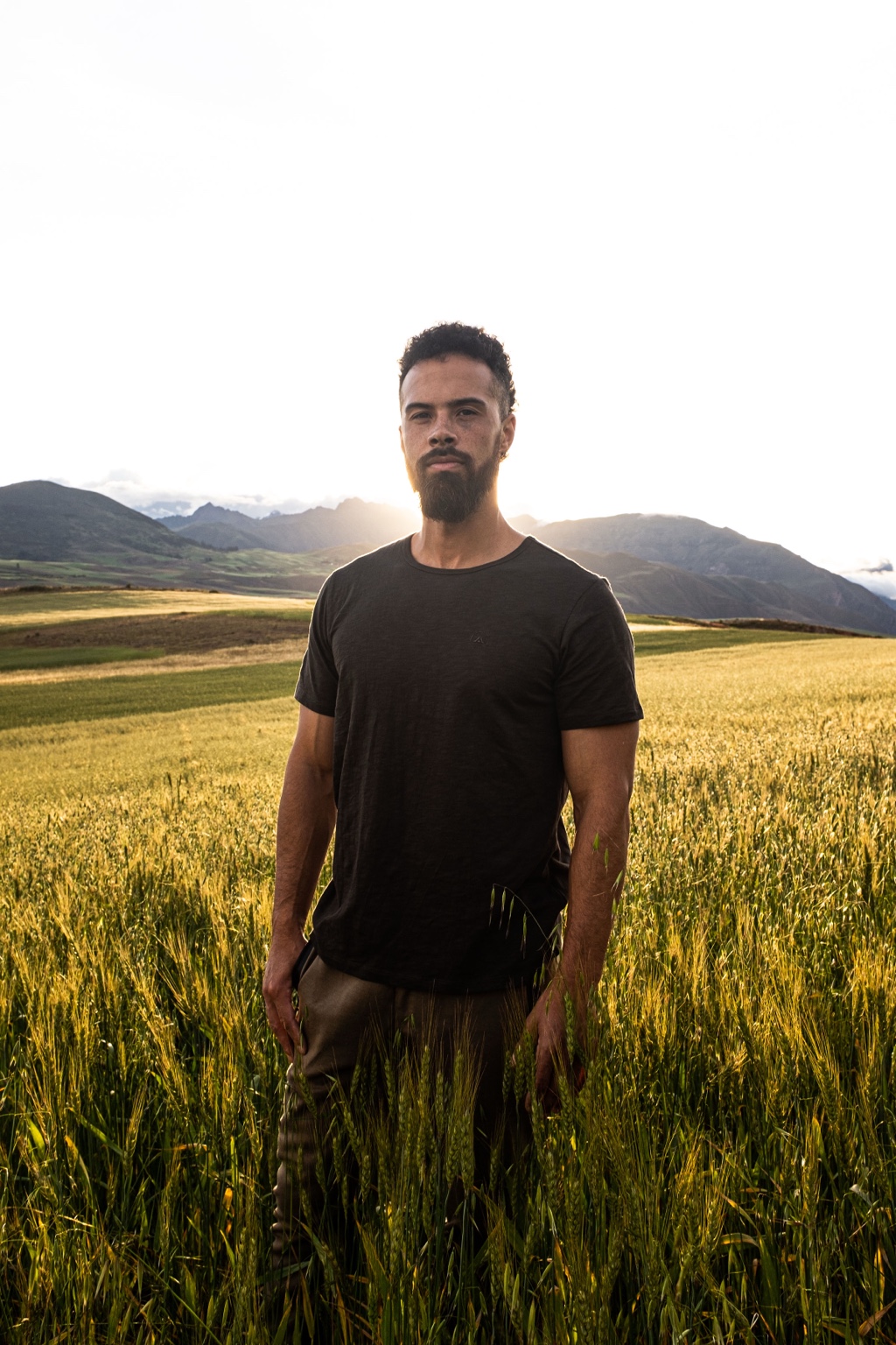Jono Mitchell standing front-facing in a golden wheat field with mountains behind him